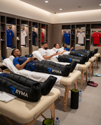 Vestiaire de club sportif : plusieurs athlètes en récupération allongés avec des bottes de pressothérapie RYMA